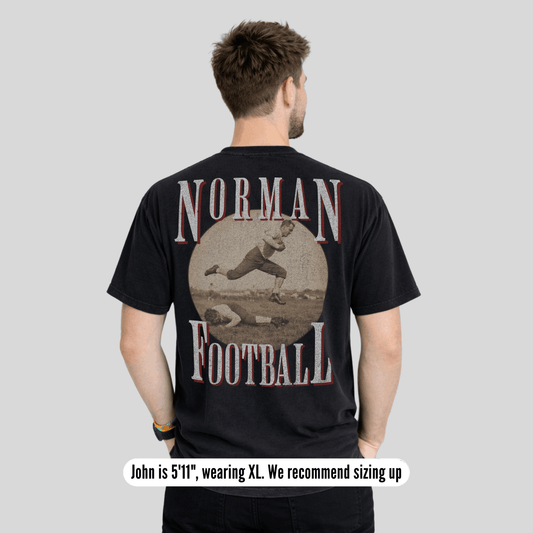 Man wearing a black t-shirt with 'Norman Football' design on the back, on a plain background.