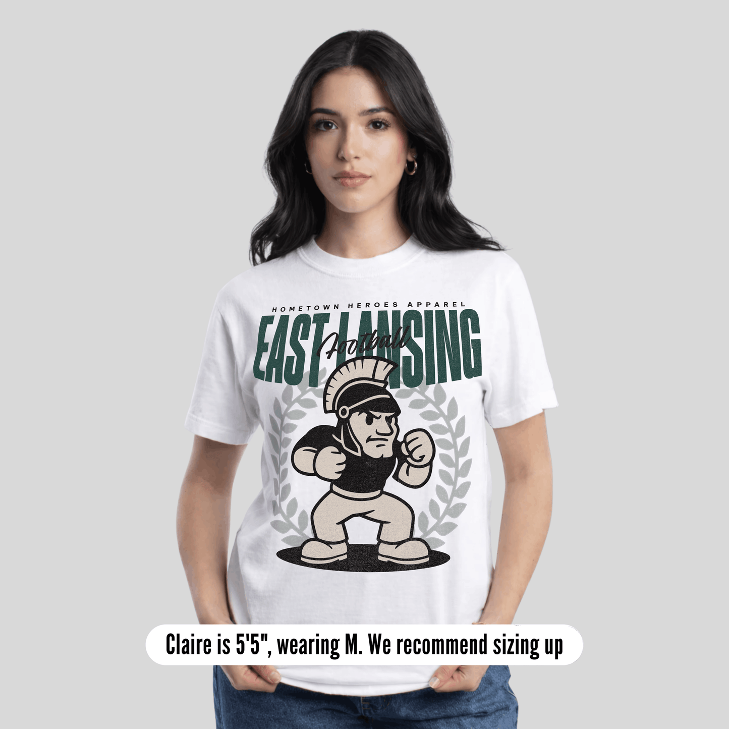 Woman wearing a white t-shirt with 'East Lansing' and a graphic design on a plain background