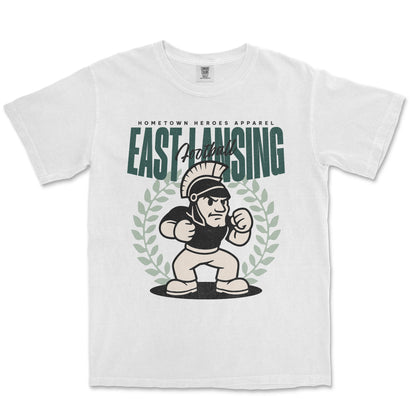White t-shirt with 'East Lansing' graphic design featuring a cartoon character and laurel wreath on a white background.