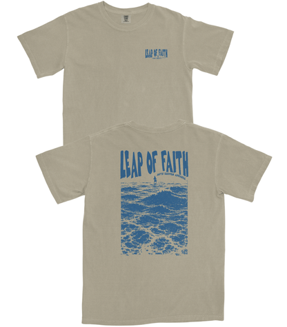 A light beige crewneck t-shirt shown from both the front and back. The front features a small blue graphic on the left chest reading 'LEAP OF FAITH'.