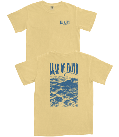 A pale yellow short-sleeve t-shirt shown from both the front and back. The front features a small blue 'Leap of Faith' logo on the left chest, while the back displays a large blue graphic of ocean waves with a lighthouse and the text 'LEAP OF FAITH' in distressed lettering.