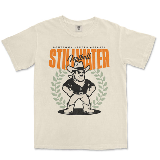 Beige t-shirt with a graphic of a cowboy and text 'Hometown Heroes Apparel Stillwater Football' on a white background
