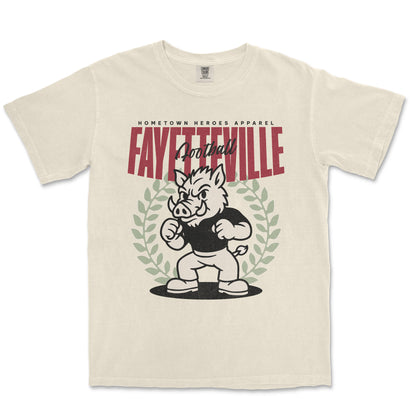 Beige t-shirt with a graphic of a boar mascot and text 'Fayetteville Football' on a white background