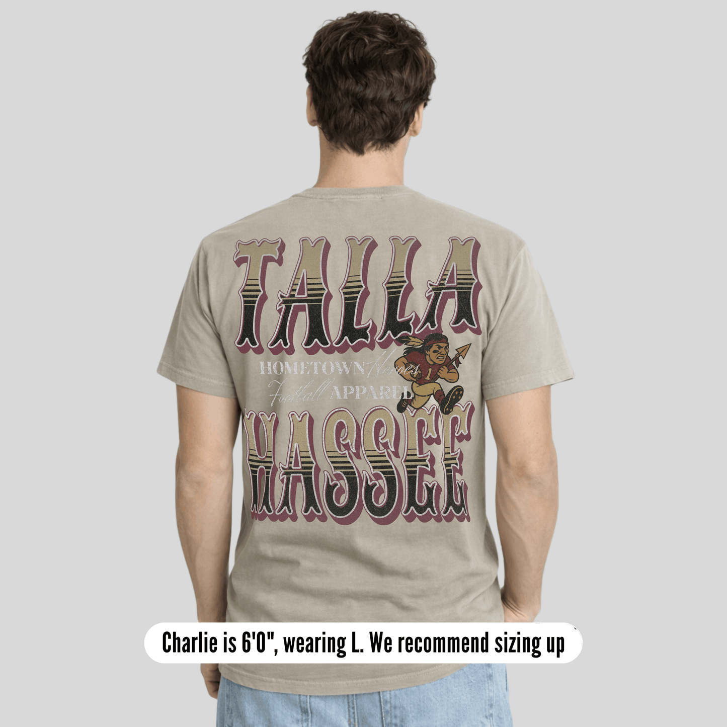 Person wearing a t-shirt with 'Talla Wassef' text and graphics on the back, standing against a plain background.