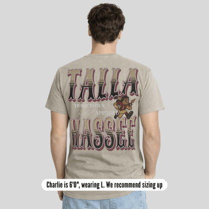 Person wearing a t-shirt with 'Talla Wassef' text and graphics on the back, standing against a plain background.