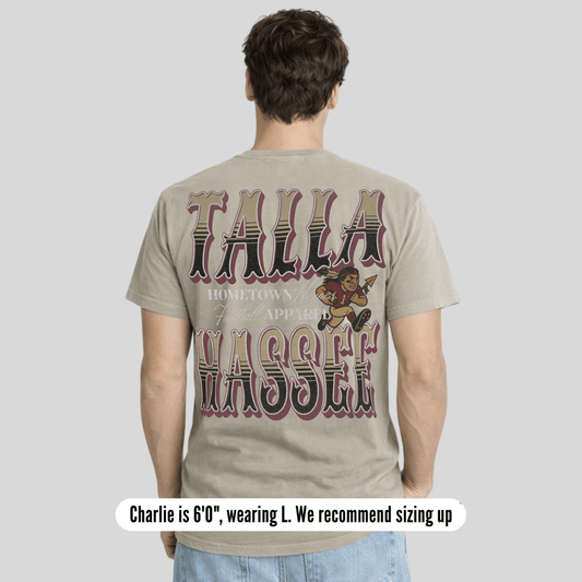 Person wearing a t-shirt with 'Talla Wassef' text and graphics on the back, standing against a plain background.