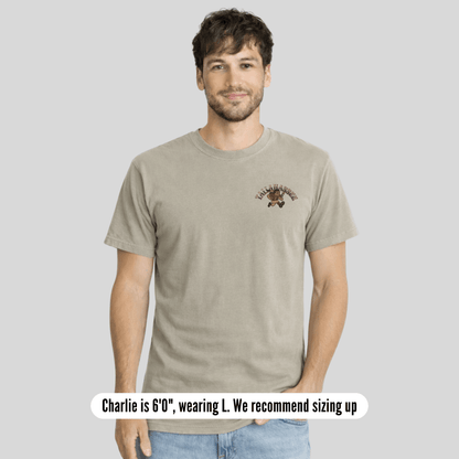 Man wearing a beige t-shirt with a logo on a plain background