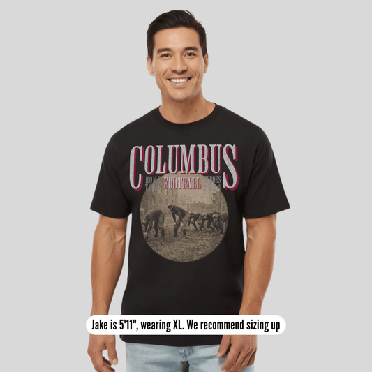 Man wearing a black t-shirt with 'Columbus' printed on it, standing against a plain background.