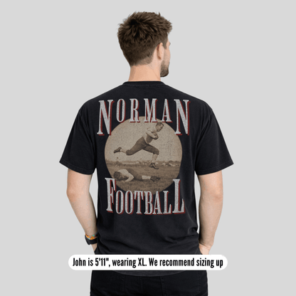 Man wearing a black t-shirt with 'Norman Football' design on the back, on a plain background.