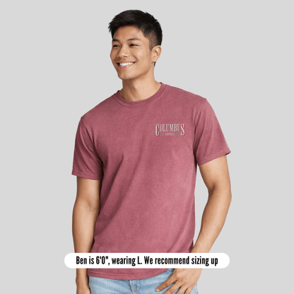 Man wearing a maroon t-shirt with 'Columbus' logo on a gray background