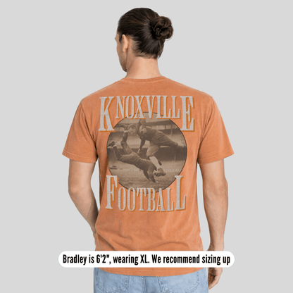 Person wearing a brown t-shirt with 'Knoxville Football' print on the back, standing against a plain background.