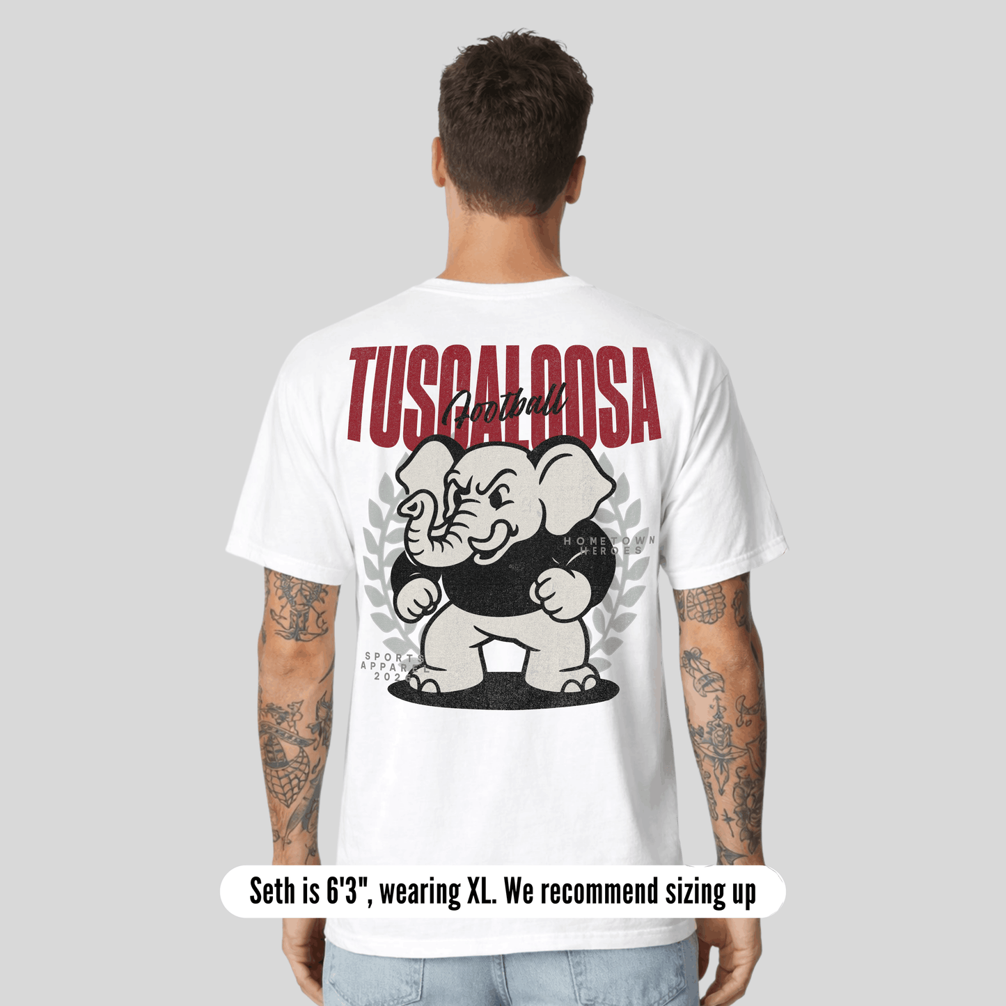 Person wearing a white t-shirt with 'Tuscaloosa' and an elephant graphic on the back, on a light gray background.
