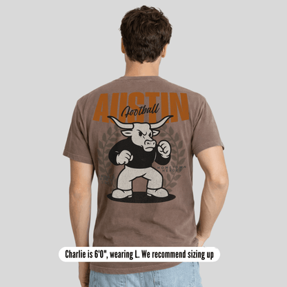 Man wearing a brown t-shirt with a graphic design on the back, standing against a plain background.