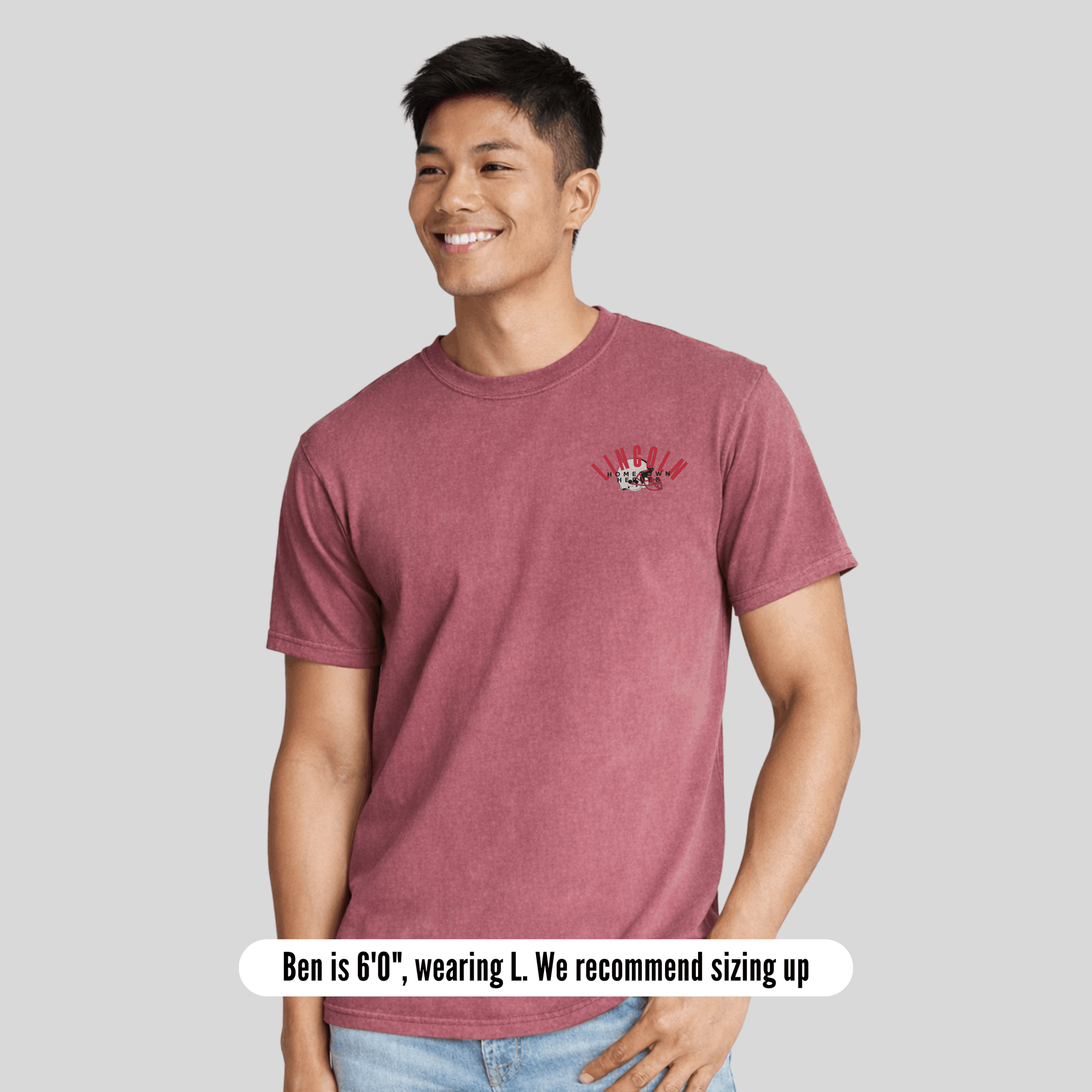 Man wearing a maroon t-shirt with a small graphic on a gray background