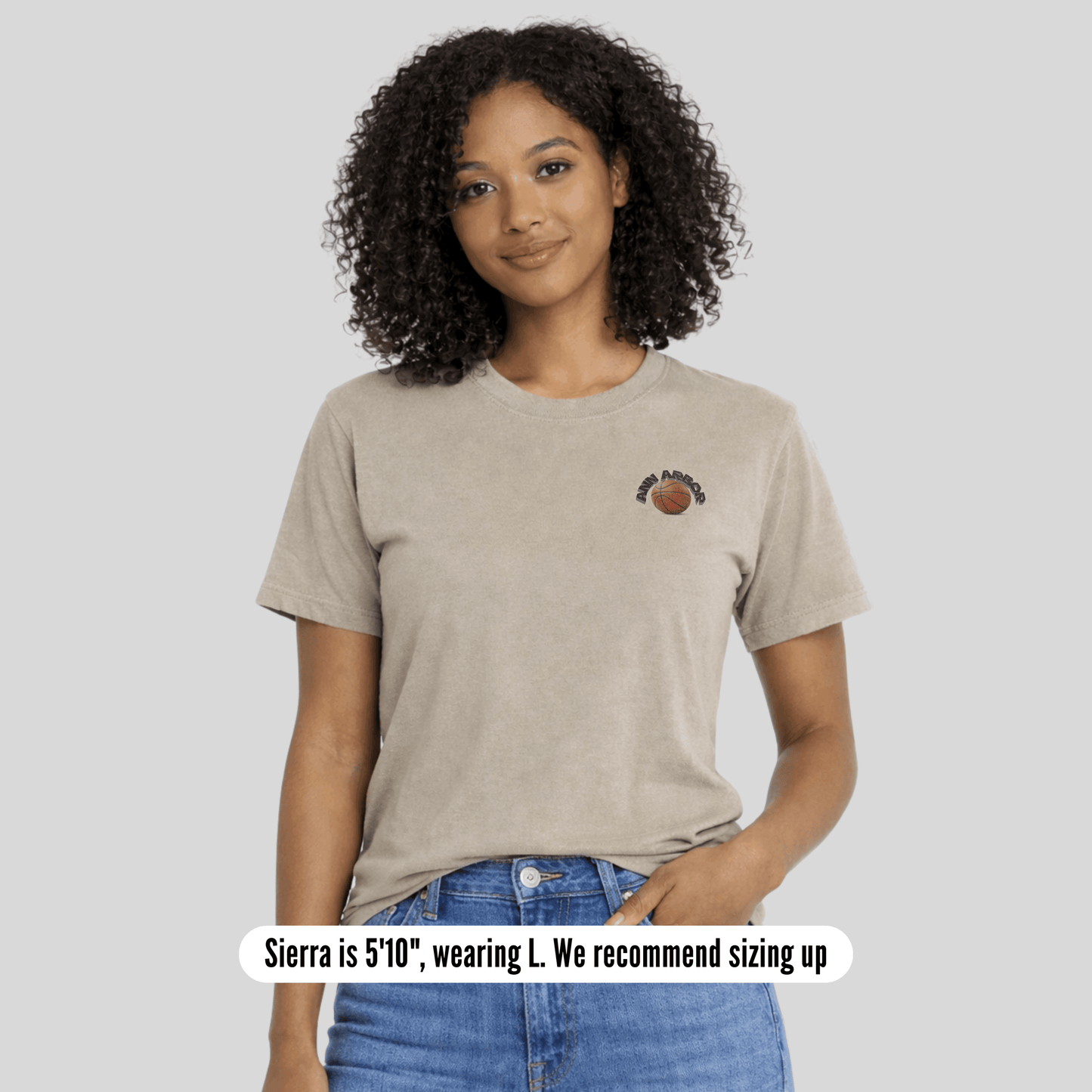 Woman wearing a beige t-shirt with a small graphic on a plain background