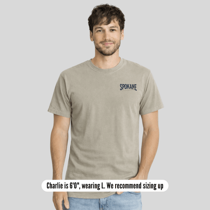 Man wearing a beige t-shirt with 'Spokane' text on a plain background