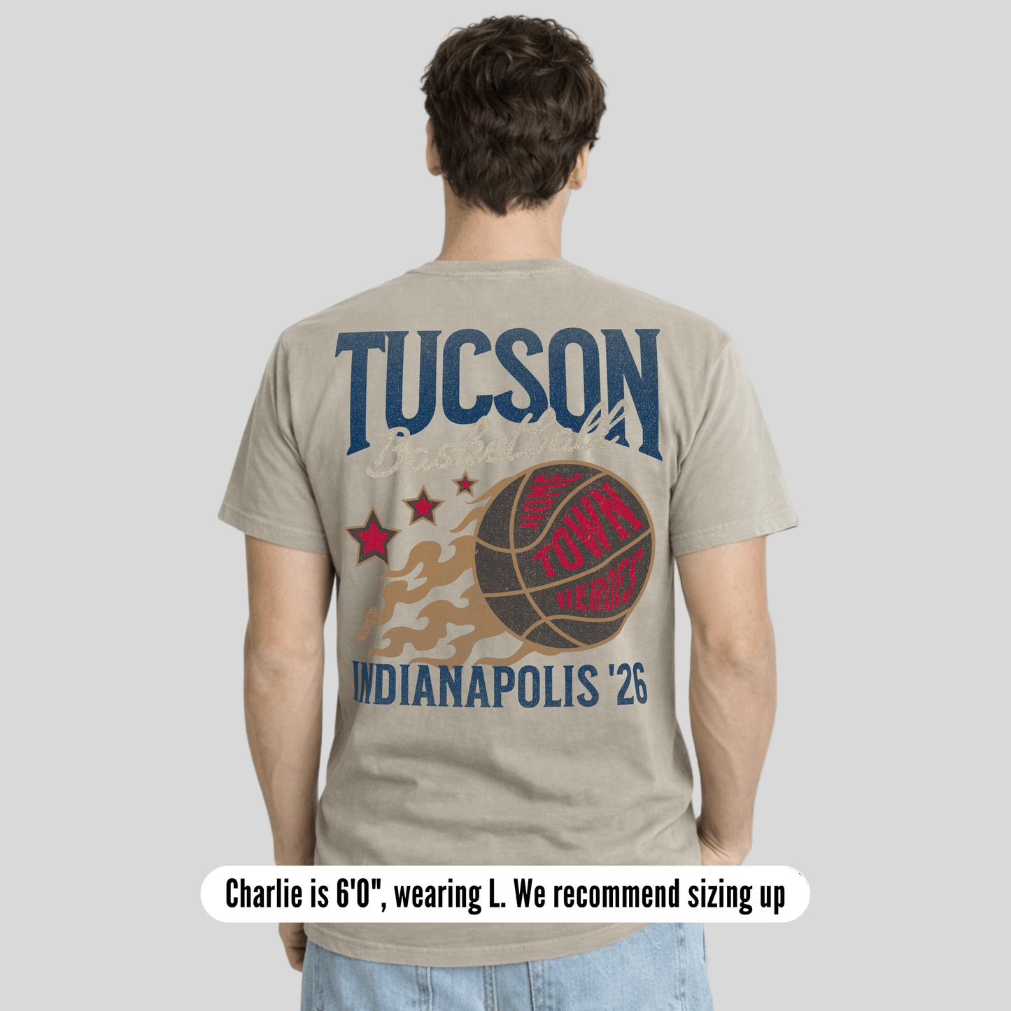 Person wearing a beige t-shirt with 'Tucson' and 'Indianapolis '26' text on the back, on a light gray background.