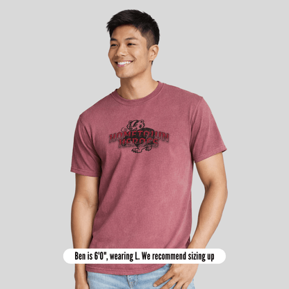 Person wearing a maroon t-shirt with a logo on a gray background